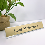 Gold nameplate with 'Lord Melbourne' text on a white surface with a plant in the background