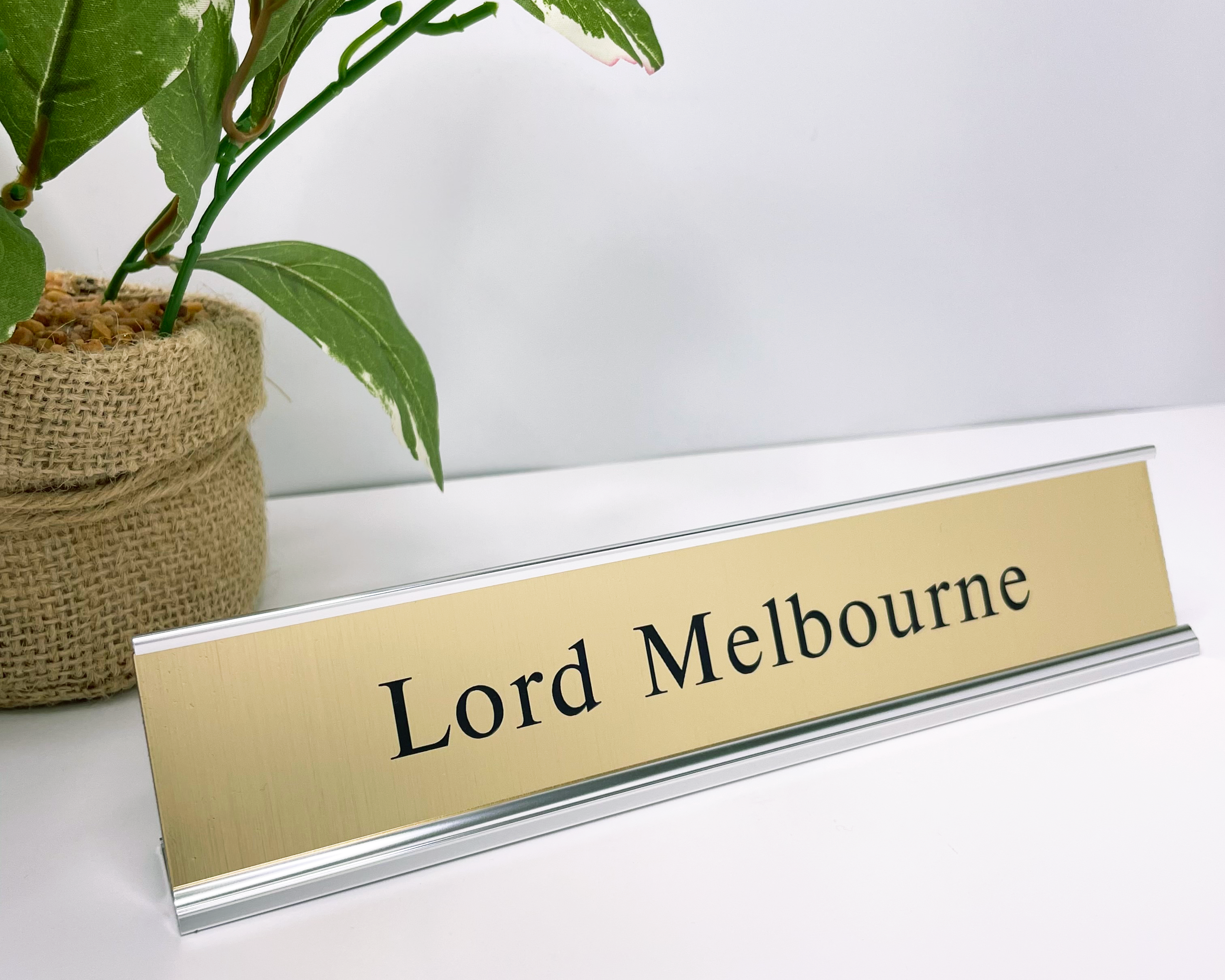 Gold nameplate with 'Lord Melbourne' text on a white surface with a plant in the background
