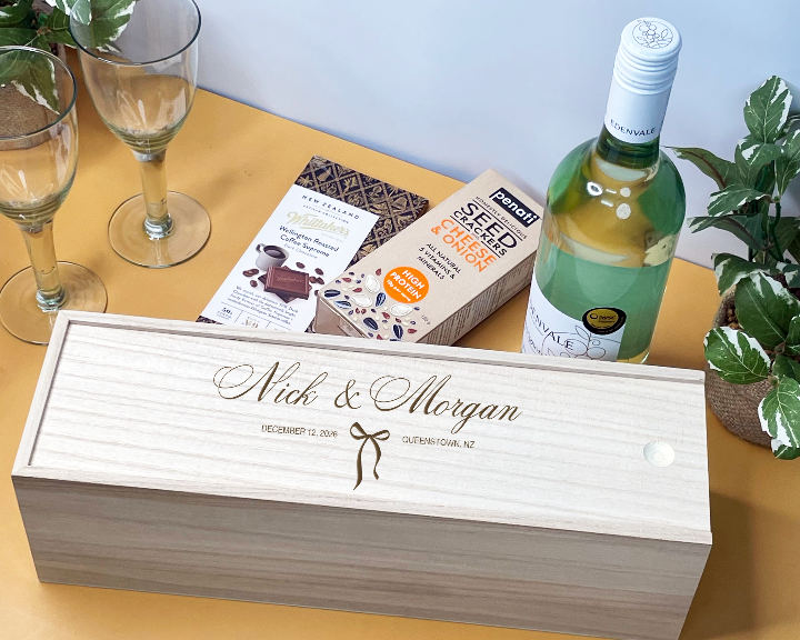 Personalized wooden Wedding Wine box with a bottle of wine on a table with glasses and plants.