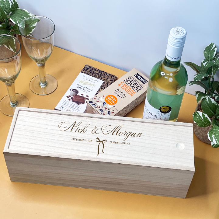 Personalized wooden Wedding Wine box with a bottle of wine on a table with glasses and plants.
