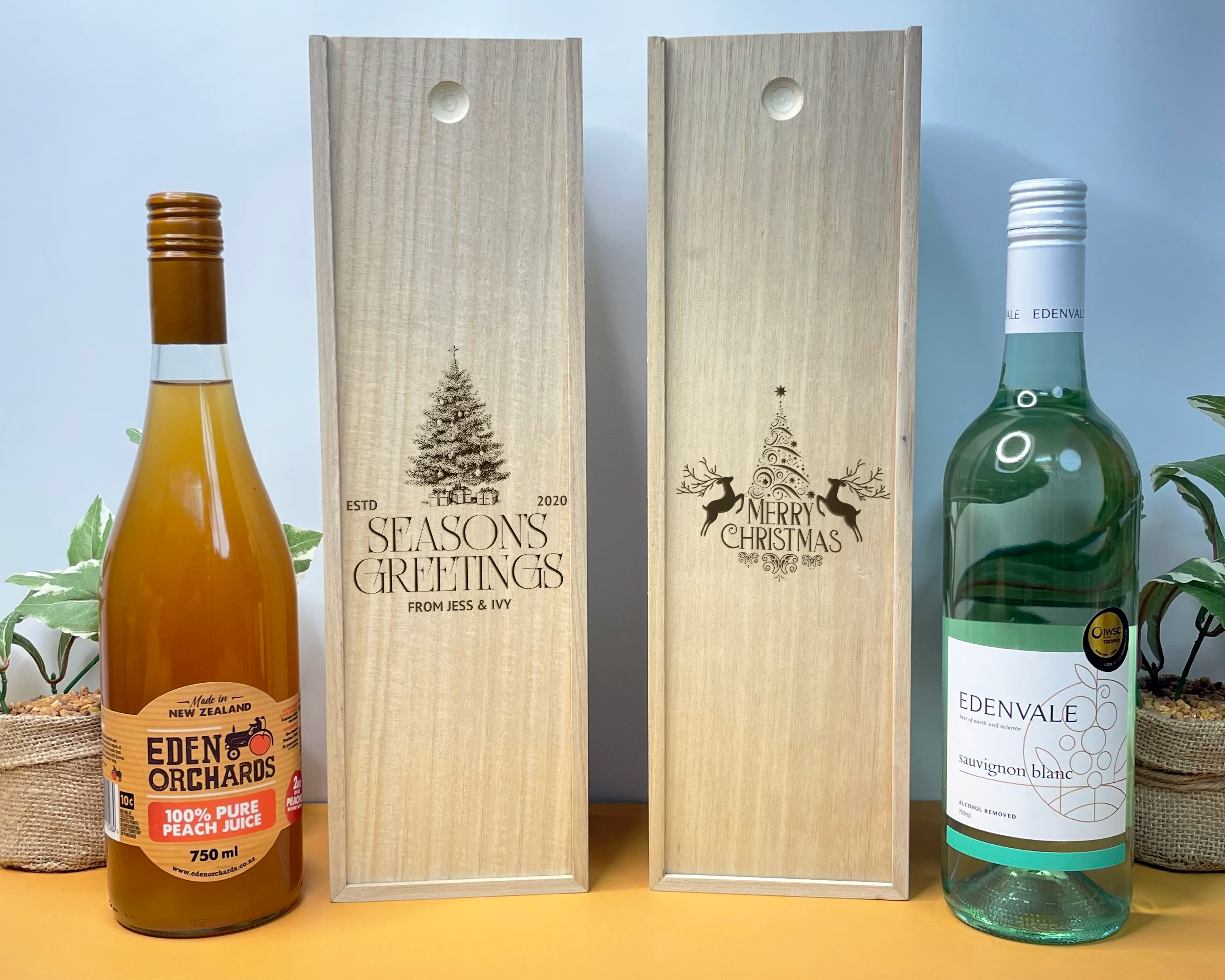 Two wooden christmas wine boxes with engraved designs next to two bottles of Eden Orchards juice and Edenvale wine.