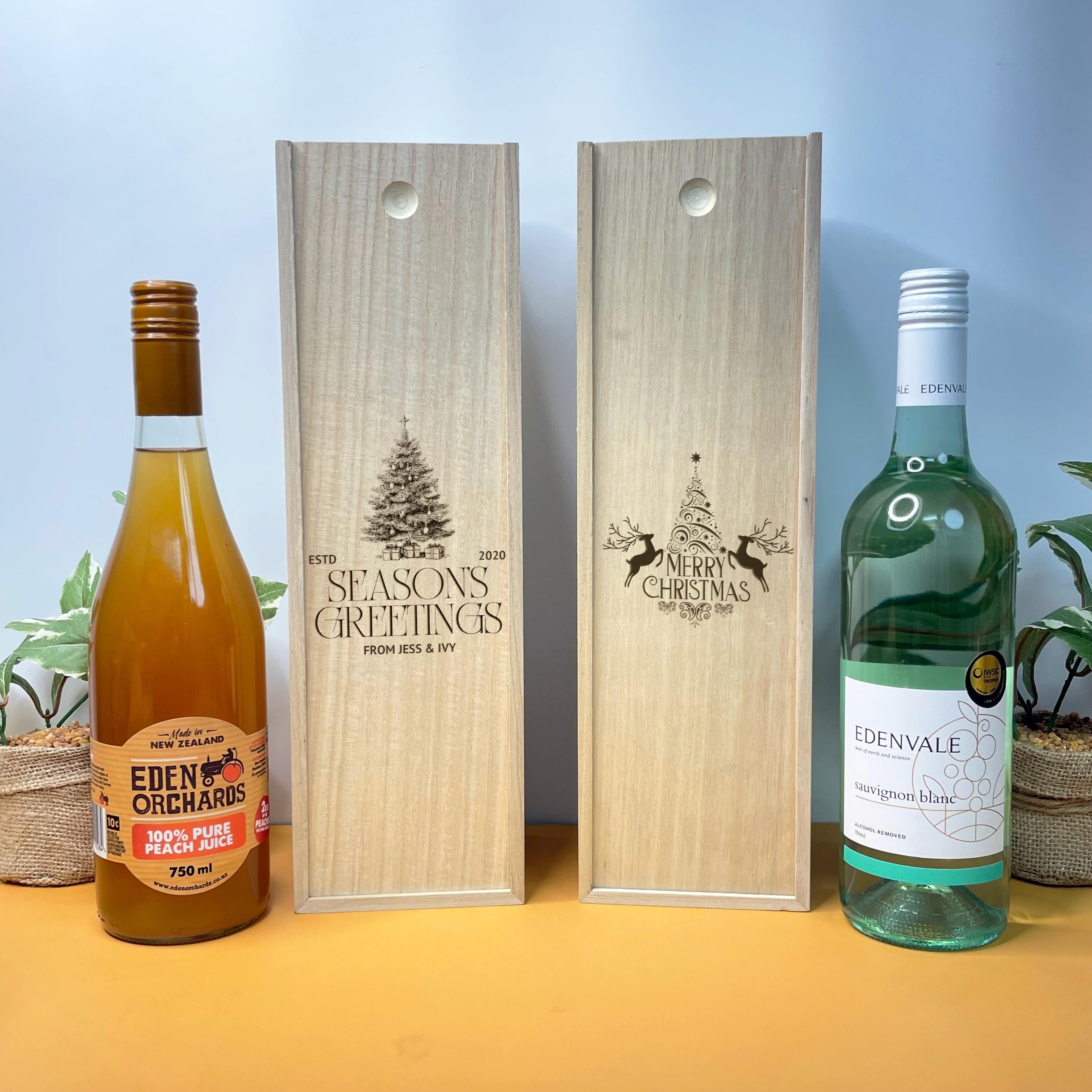 Two wooden christmas wine boxes with engraved designs next to two bottles of Eden Orchards juice and Edenvale wine.