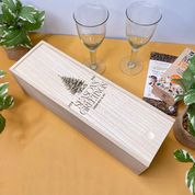 Wooden gift christmas wine box engraved with 'Season's Greetings' text on a table with wine glasses and plants.