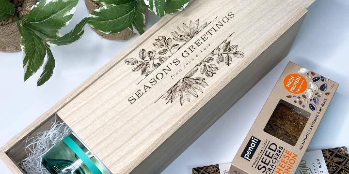 Wooden gift christmas wine box with 'Season's Greetings' text, surrounded by plants and a box of Pantry Seed, Coffee & Co. products.