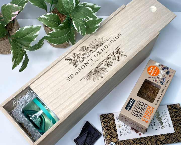 Wooden gift christmas wine box with 'Season's Greetings' text, surrounded by plants and a box of Pantry Seed, Coffee & Co. products.