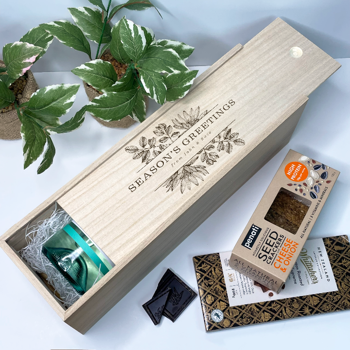 Wooden gift christmas wine box with 'Season's Greetings' text, surrounded by plants and a box of Pantry Seed, Coffee & Co. products.